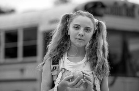 Foto de Chica de la escuela en la parte delantera del autobús escolar con manzana - Imagen libre de derechos