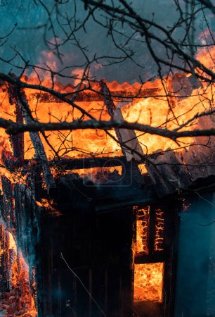 Téléchargez les photos : Brûlé dans la maison de la flamme la nuit. Incendie partout et fumée dans un quartier résidentiel la nuit. Un feu dangereux. Toute la maison et la cour en feu. Un incendie détruit une maison carbonisée brûlée - en image libre de droit