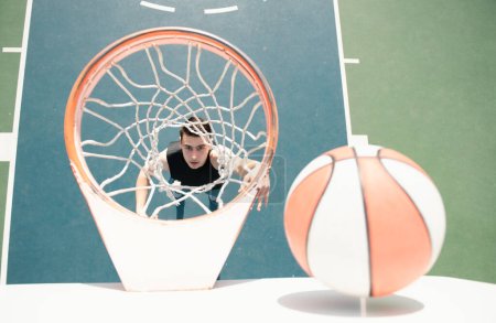 Foto de Jugador de baloncesto. Deportes y baloncesto. Un joven salta y lanza una pelota a la canasta. Cielo azul y corte en el fondo - Imagen libre de derechos