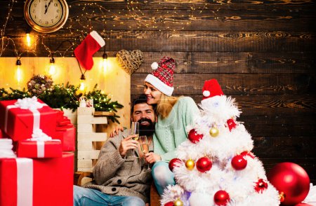 Téléchargez les photos : Un couple fête le nouvel an. Les gens d'hiver portent le chapeau rouge du Père Noël. Arbre de Noël décorer à la maison. Bonne année. Joyeux couple de Noël - en image libre de droit