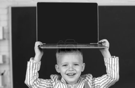 Photo for Close up portrait of child holding laptop on head, gadgets to study. Computer education for kids - Royalty Free Image