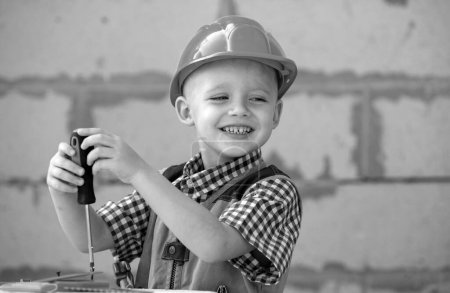 Foto de Un niño sosteniendo un destornillador. Feliz niño sonriente gira perno con destornillador. Pequeño reparador con herramienta de reparación. Lindo chico como trabajador de la construcción. Los niños juegan con destornillador - Imagen libre de derechos