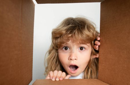 Photo for Happy little child boy is opening gift and looking inside cardboard box. Open box and delivery parcel for children - Royalty Free Image
