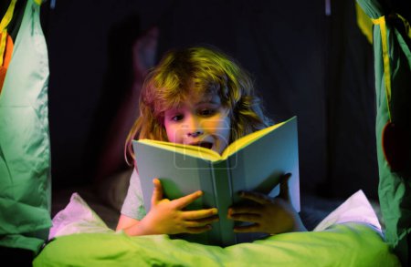 Téléchargez les photos : Excité enfant garçon livre de lecture. Les enfants lisent des histoires. C'est l'heure du coucher. Garçon lire livre dans le lit - en image libre de droit