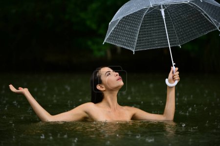 Téléchargez les photos : Femme nue sexy avec parapluie dans l'eau. Pluie estivale. Météo pluvieuse. La pluie s'en va. Femme sexy sensuellement relaxant dans l'eau. Loisirs bien être et bien-être. Pluie sensuelle. Sexy humide corps féminin - en image libre de droit