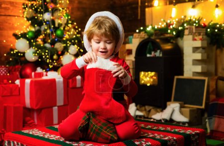 Foto de Niño de Navidad. Feliz niño sonriente con calcetines de Navidad y caja de regalo. Concepto de vacaciones. Niño feliz divirtiéndose con el regalo - Imagen libre de derechos