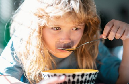 Téléchargez les photos : Cute child eats food itself with spoon. Little kid are eating soup, closeup kids face - en image libre de droit