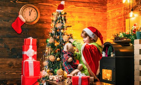 Téléchargez les photos : Joli garçon jouer près de l'arbre de Noël. Les enfants apprécient les vacances d'hiver à la maison. Maison remplie de joie et d'amour. Fais un vœu. Meilleurs voeux pour vous votre famille ce Noël. Joyeux Noël et bonne année. - en image libre de droit