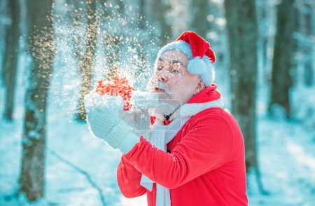 Photo for Santa blowing snow - funny face. Santa Claus coming to the winter forest with a bag of gifts on snow landscape. Santa in the winter field - Royalty Free Image