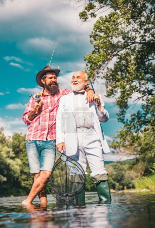 Téléchargez les photos : Père et fils mature pêcheur pêche avec une canne à pêche sur la rivière - en image libre de droit