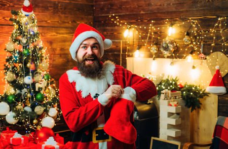 Téléchargez les photos : Bas de Noël. Styling Santa hipster avec une longue barbe posant sur le fond en bois de Noël. Émotion hivernale - en image libre de droit