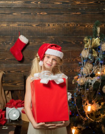 Téléchargez les photos : Décoration d'arbre de Noël. Cadeau d'enfants. Petite fille avec un cadeau de Noël sur fond en bois. Des enfants heureux. Les enfants d'hiver. Carte de Noël. Enfants de Noël - en image libre de droit