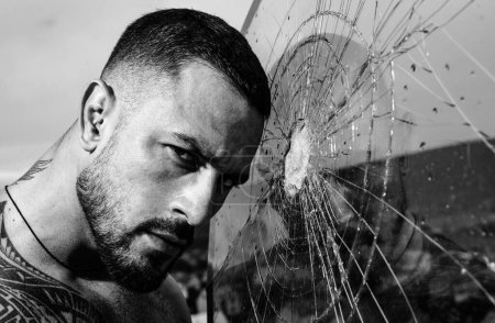 Photo for Brain destruction. crush test. theft. emotional discharge. anger. destruction. sexy hispanic man broken mirror. bullet hole in glass. broken glass because of hit. macho man behind crushed glass. - Royalty Free Image