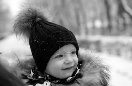 Téléchargez les photos : Bébé riant drôle en hiver dehors. Mignon enfant en bas âge dans une combinaison de neige chaude et chapeau découvert forêt d'hiver. Neige, joues rouges, sourire sur le visage - en image libre de droit