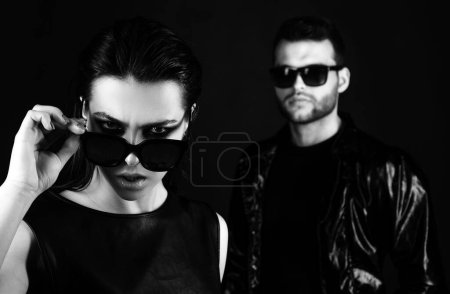 Photo for Boy in suits and a girl in an black glasses. Fashion photo of handsome man and woman. Man and woman on serious faces. Company of confident people friends. Isolated on black - Royalty Free Image