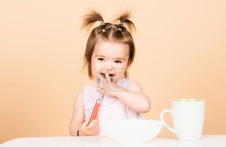 Photo for Babies eating, healthy food for a baby. Smiling baby girl with spoon on studio, isolated - Royalty Free Image
