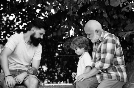 Foto de El abuelo y el nieto están jugando ajedrez y sonriendo mientras pasan tiempo juntos en el parque. Hombre feliz concepto de familia jugando al Ajedrez y divertirse juntos - Imagen libre de derechos