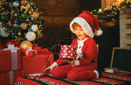 Foto de Niño sorprendido con la cara alegre consiguió regalo en la caja de Navidad. Concepto de alegría y felicidad. Celebrando la Navidad en interiores. Santa ayudante. Feliz Año Nuevo y Feliz Navidad - Imagen libre de derechos