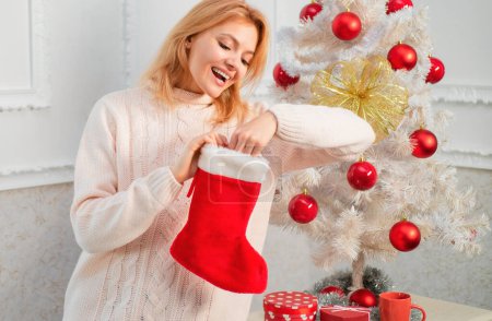 Foto de Mujer con calcetín de Navidad. Medias de Navidad. Mujer joven con cajas de regalo de Navidad delante del árbol de Navidad. Feliz año nuevo. Regalo de año nuevo - Imagen libre de derechos