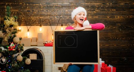 Photo for Christmas Woman holding a black desk for text. Black board copyspace. Sexy Santa woman posing on vintage wooden background. Woman holding a black desk for text. Black board copy space. Sensual young - Royalty Free Image