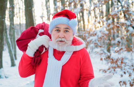 Téléchargez les photos : Drôle de Père Noël venir à la forêt d'hiver avec un sac de cadeaux, paysage de neige - en image libre de droit