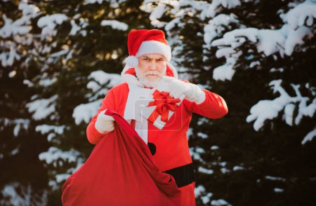 Téléchargez les photos : Paysage hivernal de forêt et de neige avec Santa Claus. Joyeux Noël. Le Père Noël la veille de Noël porte des cadeaux aux enfants dans un sac rouge - en image libre de droit