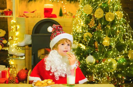 Téléchargez les photos : Père Noël tenant des biscuits de Noël et du lait sur fond d'arbre de Noël. Biscuits pour enfants Père Noël. Enfant Père Noël profiter dans le gâteau au pain d'épice servi et le lait - en image libre de droit