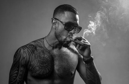 Photo for Muscular macho man with athletic body. sexy abs of tattoo man. sport and fitness, health. confidence charisma. brutal sportsman torso. steroids. smoking cigarette. exhale smoke. bad habit. harmful. - Royalty Free Image