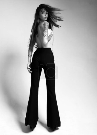 Photo for Tall slim lady. Topless model wear high waist pants. Tattooed sensual model long hair. Fashion concept. Windy hairstyle. Girl attractive fashion model. Vogue and fashion. Gorgeous pretty woman. - Royalty Free Image