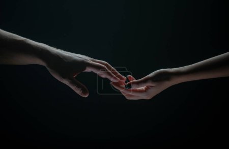 Two hands stretch each other, black background. Couple in love holding hads, close up. Helping hand, support, friendship