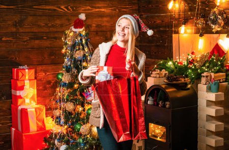 Photo for Happy shopping. Noel. Girl enjoy cozy atmosphere christmas eve. Pleasant moments. Christmas joy. Woman wooden interior christmas decorations garland lights. Christmas tree. Happiness cheer and love. - Royalty Free Image