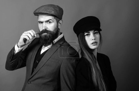Photo for Vintage retro couple on red wall. Old style hat on bearded man and black fashion cap on beauty woman - Royalty Free Image