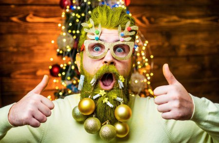 Foto de Retrato de moda de hombre guapo en el interior con árbol de Navidad. Concepto de año nuevo. Sexy hombre de Santa posando sobre fondo de madera vintage - Imagen libre de derechos