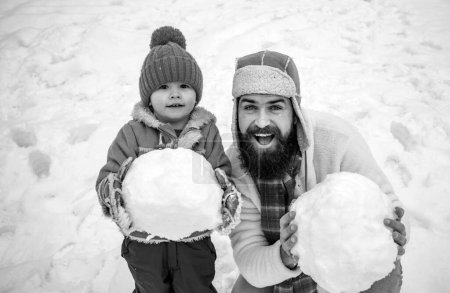 Téléchargez les photos : Papa et bébé fils jouent ensemble à l'extérieur. Père et fils d'hiver. Enfant heureux jouant avec boule de neige sur fond blanc d'hiver. Scène d'hiver sur fond de neige blanche - en image libre de droit