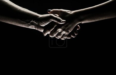 Foto de Handshake between the two partners. Rescue or helping gesture of hands. Concept of salvation. Hands of two people at the time of rescue, agreement, help. Isolated on black background - Imagen libre de derechos
