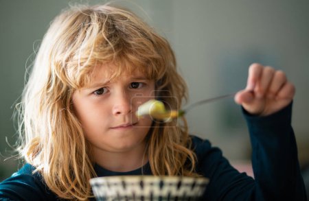 Téléchargez les photos : Close up portrait of funny kid eating. Sad boy eating healthy chicken noodle soup for lunch. Unhappy baby child taking food at home or nursery daycare or kindergarten - en image libre de droit