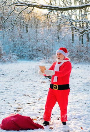 Téléchargez les photos : Funny Santa lire la liste de souhaits sur la veille de Noël à l'extérieur - en image libre de droit