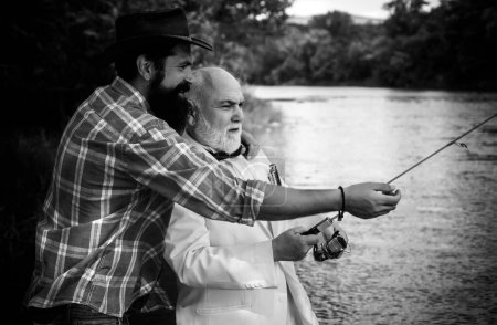 Téléchargez les photos : Fly rod and reel avec une truite brune d'un ruisseau. Père et fils se relaxent ensemble. Hommes pêchant dans la rivière pendant la journée d'été. Pêche homme - en image libre de droit
