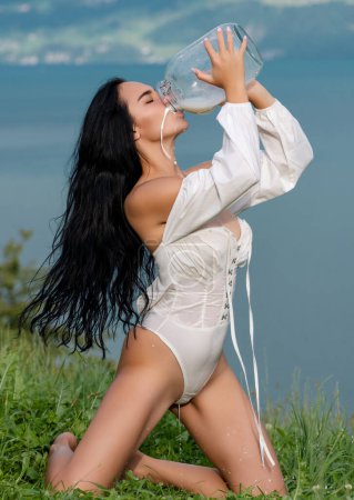 Photo for Sexy woman in sexy lingerie on farm. Girl drink milk from bottle. Woman drink raw milk at countryside. Fresh milk. Female mouth with dripping milk. Sensual woman with milky splashes. Country girl - Royalty Free Image