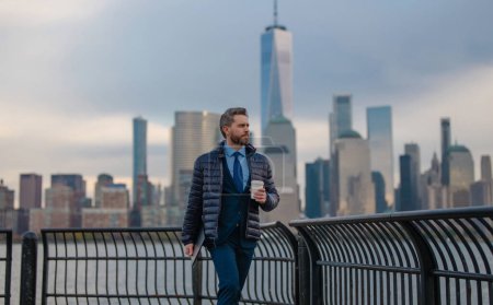 Foto de Un hombre de negocios con chaqueta caliente bebe café en Nueva York. Hombre de negocios en otoño Nueva York, Manhattan. Hombre de negocios guapo afuera en otoño. Hombre maduro en chaqueta caminando y beber tomar tomar café - Imagen libre de derechos