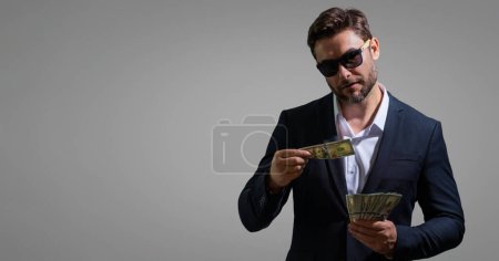 Photo for Man holding cash money in dollar banknotes on isolated gray background. Studio portrait of businessman with bunch of dollar banknotes. Dollar money concept. Career wealth business. Cash dollar banner - Royalty Free Image