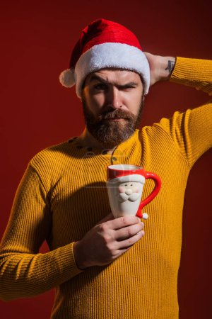 Photo for Santas face. Bearded man in Santa hats on red studio background. Santa celebration Happy New Year and Christmas winter holiday. Portrait of Santa with cup. Man beard in Santa costume with cup - Royalty Free Image