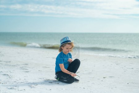 Photo for Kid boy drawing family on a sand on summer beach. Little kid on summer vacations. Happy child drawing with bamboo stick on the sand rest on sea. Summer vacation concept. Kids summer travel and - Royalty Free Image