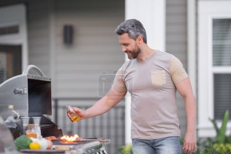 Téléchargez les photos : Homme hispanique cuisinant sur le barbecue dans la cour arrière. Chef préparant le barbecue. Chef cuisinier de barbecue. Charmant homme préparant barbecue, viande barbecue. Grill et barbecue - en image libre de droit
