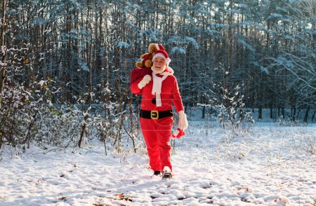 Téléchargez les photos : Père Noël dans le champ d'hiver. Père Noël la veille de Noël est portant des cadeaux aux enfants dans un sac pleine longueur - en image libre de droit