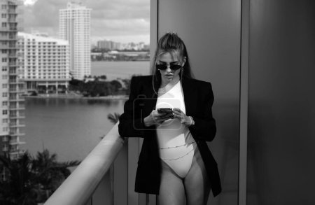 Foto de Mujer sexy escribiendo un mensaje en el teléfono. Sexy mujer de negocios en traje y gafas de sol charlando en el teléfono inteligente - Imagen libre de derechos