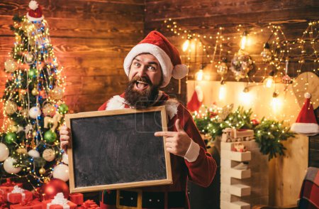 Téléchargez les photos : Hipster Santa avec panneau texte à la maison. Bonne année. Homme barbu en pull de Noël. Joyeux hiver. Drôle de Père Noël. Préparation de Noël - homme célébrant le Nouvel An - en image libre de droit