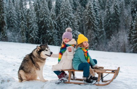Foto de Niños con perro husky en trineo. Niños y niñas juegan afuera en la nieve. Invierno, vacaciones y Navidad - Imagen libre de derechos
