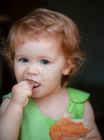 Téléchargez les photos : Portrait de bébé mignon avec du pain dans les mains en train de manger. Petit enfant mignon manger sandwich, concept d'auto-alimentation - en image libre de droit