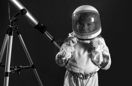 Téléchargez les photos : Concept cosmonaute pour enfants de l'espace. Portrait d'un petit garçon positif avec un télescope portant un casque avec joie. Arrière-plan isolé avec espace de copie. Concept d'astronomie et d'astrologie - en image libre de droit